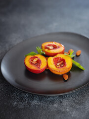 Summer dessert - Cooking Ripe grilled peaches with honey and nuts over dark plate and table. Selective focus with blurred foreground and background. closeup