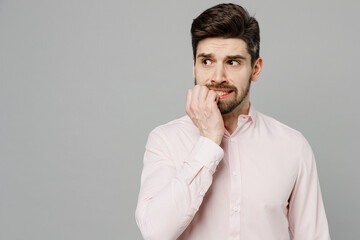 Young minded worried sad upset caucasian man 20s wear basic white shirt look aside on workspace copy space mock up area biting nails isolated on plain grey background studio People lifestyle concept.