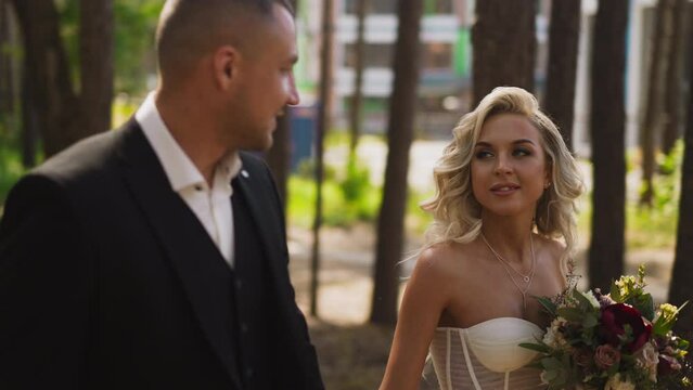 Man in suit and woman in wedding dress walk along park