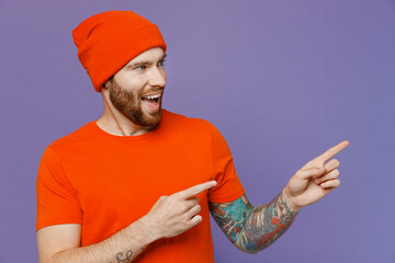 Young smiling man 20s he wear red hat t-shirt point index finger aside indicate on workspace area copy space mock up isolated on plain pastel light purple background studio. People lifestyle concept.