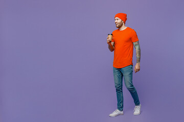 Full body young european man 20s wear red hat t-shirt hold takeaway delivery craft paper brown cup coffee to go walk isolated on plain pastel light purple background studio. People lifestyle concept.