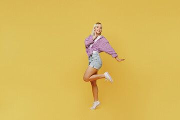 Fototapeta na wymiar Full body side view fun young blonde woman 20s she wear pink tied shirt white t-shirt look camera raise up leg hold face isolated on plain yellow background studio portrait. People lifestyle concept.
