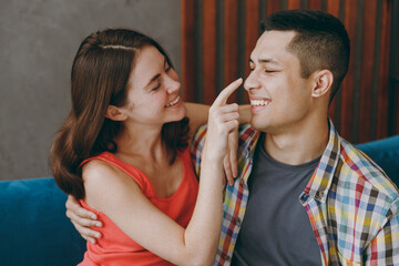 Side view cheerful happy young couple friends family man woman in casual clothes hug touch nose sits on blue sofa together stay at home flat rest spend free spare time in living room indoors grey wall