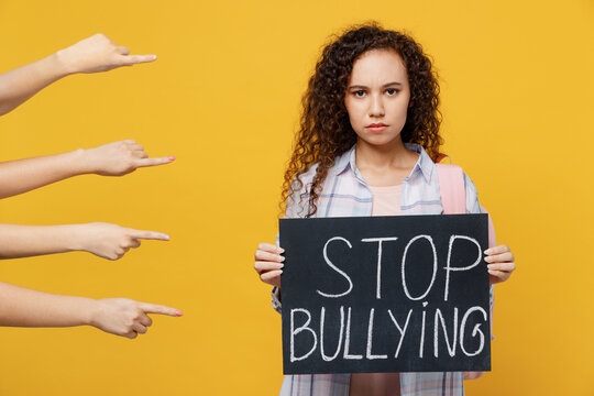 Young Sad Depressed Black Teen Girl Student She In Casual Clothes Backpack Bag Hold Card Sign With Stop Bullying Title Text Isolated On Plain Yellow Background High School University College Concept