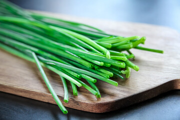 Bunch of chives on a wooden cutting board - obrazy, fototapety, plakaty