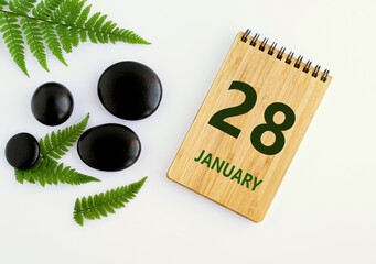 January 28. 28th day of the month, calendar date. Notepad, black stones, green leaves. Winter...