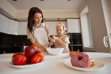 Family in the kitchen. Beautiful mother with her little daughter. A woman in an apron kneads the dough. Add flour. bake pancakes