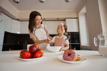 Family in the kitchen. Beautiful mother with her little daughter. A woman in an apron is kneading. Girl learning to cook dough