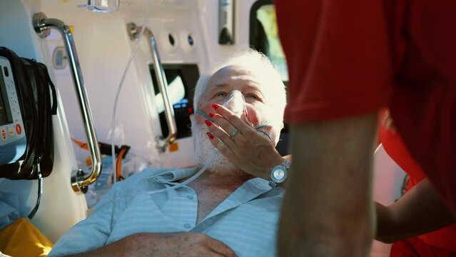 Senior male patient receiving advanced emergency medical care in ambulance. Paramedic holding patient head wearing oxygen mask in ambulance