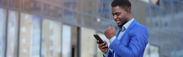 African American man happy winning tender for business after upgrading startup. Mature businessman looks for excellent results on smartphone with smile, sunlight