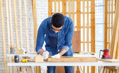 Indian Asian professional engineer architect foreman labor worker wears safety goggles glasses and gloves using square angle degree ruler measuring wood on working table in housing construction site