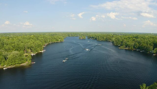 Boats and jetskis ride down a beautiful blue river on a summer day. Aerial view from drone.
