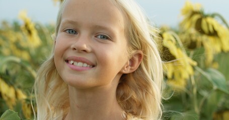 Beautiful little girl enjoying nature . Happy smiling female kid standing in sunflowers field