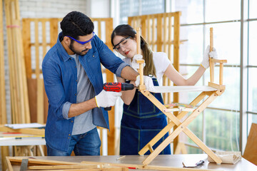 Asian professional cheerful female engineer architect foreman labor worker sitting smiling holding tablet computer discussing with Indian bearded male carpenter in workshop housing construction site