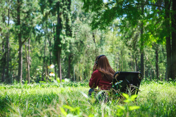 Rear view of a young woman enjoy listening to music with headphone while sitting on a camping chair in the park