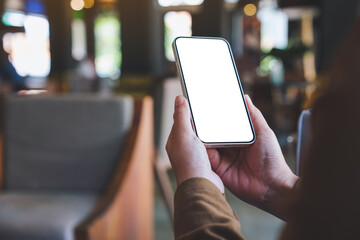 Mockup image of a woman holding mobile phone with blank desktop screen in cafe