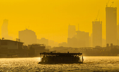 
A boat carrying people crossing the Chao Phraya River in the morning. Behind it is the Buddha Yodfa Bridge built during World War II, Bangkok, Thailand.