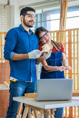 Obraz premium Asian Indian professional male and female engineer architect foreman labor worker lover couple wear safety goggles standing cuddling leaning together holding wooden home model in construction site