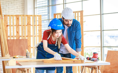 Indian romantic cheerful bearded male engineer architect foreman labor worker carpenter smiling holding Asian female girlfriend hand helping measuring wood board on table in housing construction site