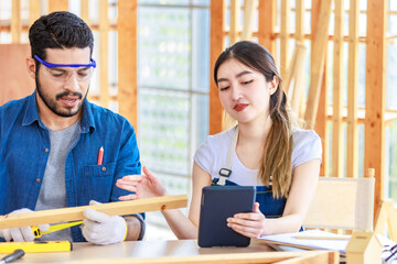 Obraz premium Asian professional cheerful female engineer architect foreman labor worker sitting smiling holding tablet computer discussing with Indian bearded male carpenter in workshop housing construction site