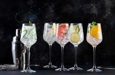 Gin tonic cocktails set in wine glasses. Trendy Alcoholic drinks with lime, lemon, grapefruit, orange, cucumber, soda and spicy herbs, black background. Summer cocktail party