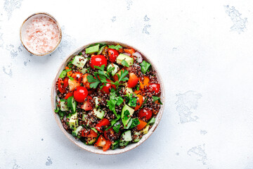 Fototapeta na wymiar Quinoa tabbouleh salad with tomatoes, paprika, avocado, cucumbers and parsley. Traditional Middle Eastern and Arabic dish. White kitchen table background, top view