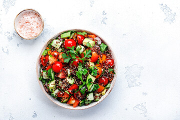 Quinoa tabbouleh salad with tomatoes, paprika, avocado, cucumbers and parsley. Traditional Middle Eastern and Arabic dish. White kitchen table background, top view