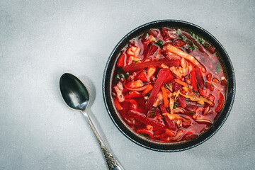 Summer Vegetable Soup with  cabbage, beets, and herbs. Russian borscht in plate on grey kitchen table background, top view, copy space. Vegan, vegetarian local food