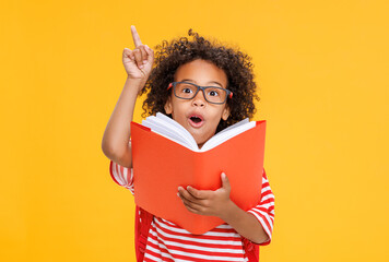 Smart ethnic schoolboy in glasses reading book