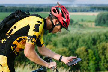 Happy male cyclist sending a text message on his mobile phone. Image of a cyclist on a mountain bike using a smartphone navigator exploring a map and searching for GPS coordinates while cycling.