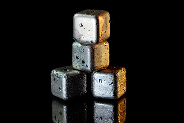 Stainless steel cubes simulating ice for cooling drinks on a black surface with a reflection.
