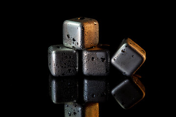 Stainless steel cubes simulating ice for cooling drinks on a black surface with a reflection.