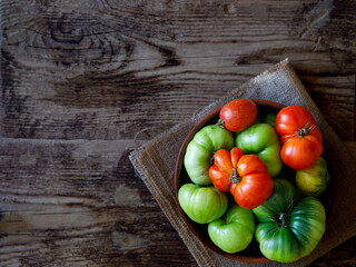 Fresh ripe and unripe organic tomatoes in bowl on rustic dark wooden table top view copy space. Tomato red and green background healthy food vegetables on old board.