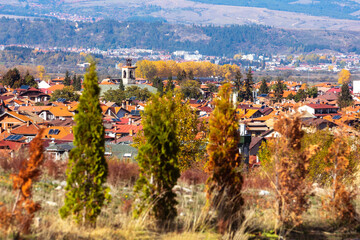 Bansko, Bulgaria town panorama with houses roofs, church and colorful autumn trees