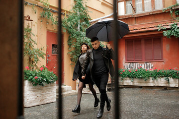 The sweet couple running in the yard under an umbrella in rainy weather. November 2, 2019, Lviv, Ukraine.