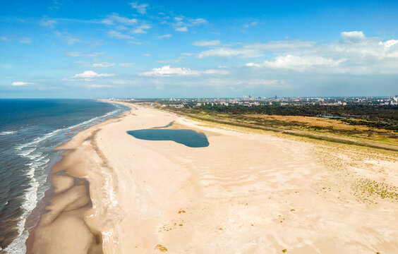 Aerial photo of the Zand Motor peninsula of the Kijkduin Beach of The Hague. In the background a large rain shower cloud and the city of The Hague skyline