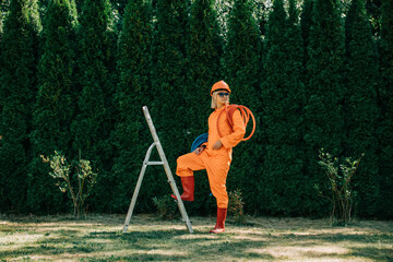 Stylish woman in orange suit, hardhat, pipes and sunglasses next to stepladder