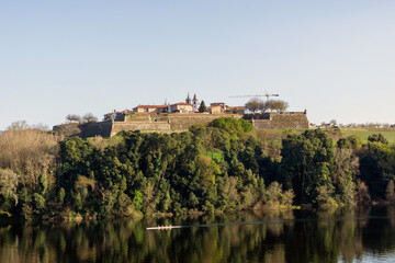 Fototapeta na wymiar Fortaleza de Valença de Miño. En el río Miño se reflejan los árboles y pasa una piragua.