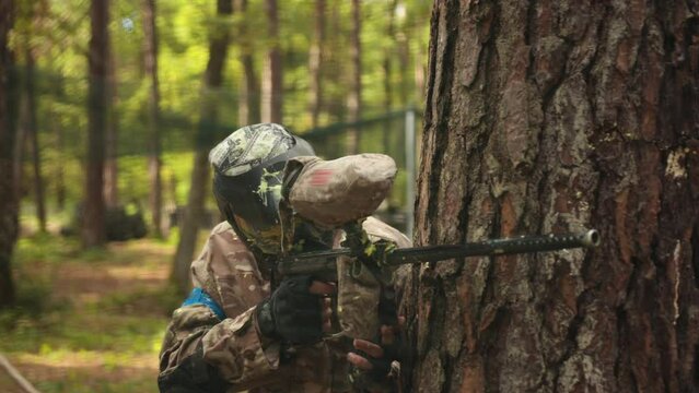 A young man wearing camouflage and a protective mask plays paintball battles with his friends while at his leisure activity.