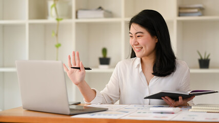 Fototapeta na wymiar Smiling asian female entrepreneur making video call with her business partner, watching online webinar on laptop computer