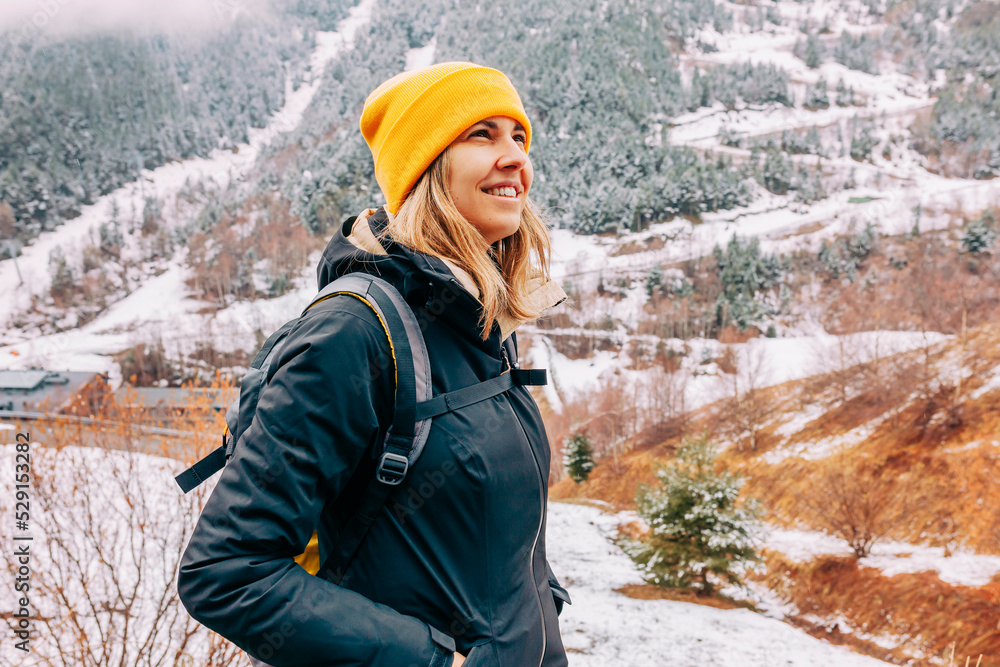 Wall mural Winter hike on snow mountain young happy hiker woman climbing. Europe travel adventure trek in nature landscape. Young cheerful female wearing yellow hat, black jacket for cold weather and bag.