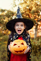 A child girl in a witch costume holds a pumpkin in her hands.  Halloween celebration.
