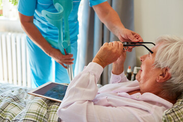 Krankenschwester gibt kranker Seniorin im Bett eine Brille