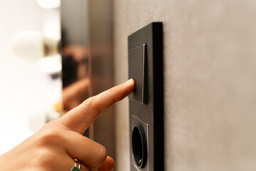 woman's hand turning off the light switch with a finger. concept turn off the light for energy...