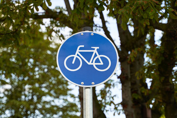 Road signs for cyclists. Bike visible on blue sign. Nature out of focus visible in the background. Environmentally conscious mobility.  