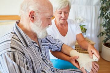 Pflegekraft beim Verband anlegen am Handgelenk von Senior