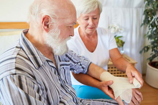 Pflegekraft beim Verband anlegen am Handgelenk von Senior