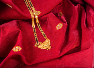 Fototapeta na wymiar Mangalsutra or Golden Necklace to wear by a married hindu women, arranged with traditional saree with haldi, kumkum and flowers on plate.