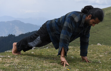 Full length of a Indian young man with ponytail hair doing three finger push ups in the top of...