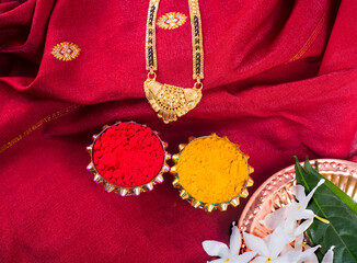 Mangalsutra or Golden Necklace to wear by a married hindu women, arranged with traditional saree with haldi, kumkum and flowers on plate.